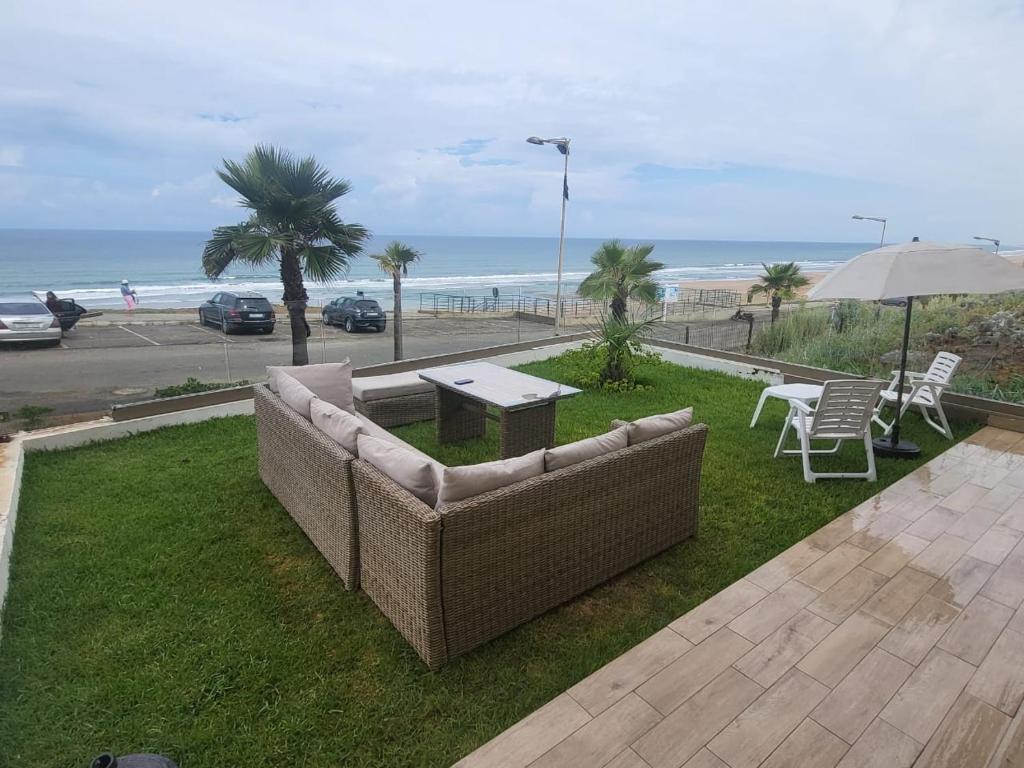 Appartement Plage des Nations Prestigia Front Mer avec grand Jardin في Sidi Bouqnadel: أريكة للجلوس على العشب بالقرب من الشاطئ