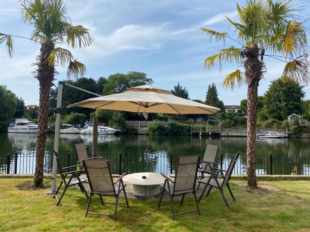 a table with chairs and an umbrella next to a lake at Riverside 4 Bedroom House Wraysbury Staines in Wraysbury