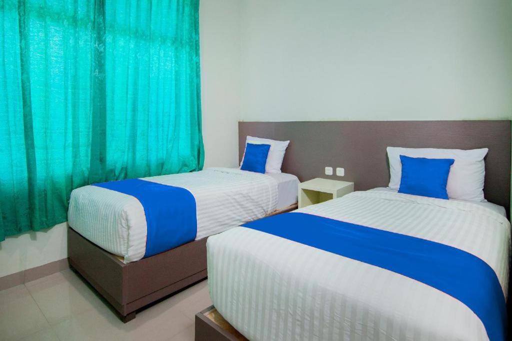 two beds in a hotel room with blue curtains at Hotel Wisata Samosir By Helocus in Pangururan