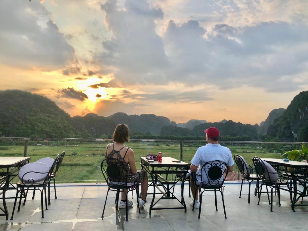 un hombre y una mujer sentados en las mesas viendo la puesta de sol en Liberty Hall Tam Coc Hotel & Villa, en Ninh Binh