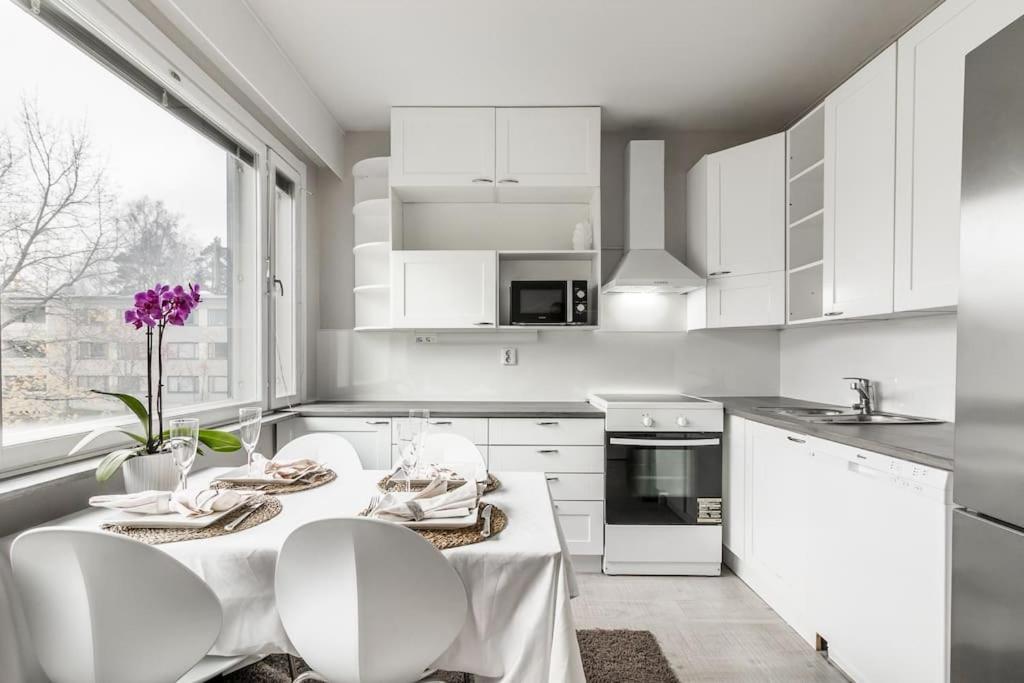a kitchen with white cabinets and a table and chairs at Upea 2 makuuhuoneen huoneisto lähellä lentokenttää! in Vantaa