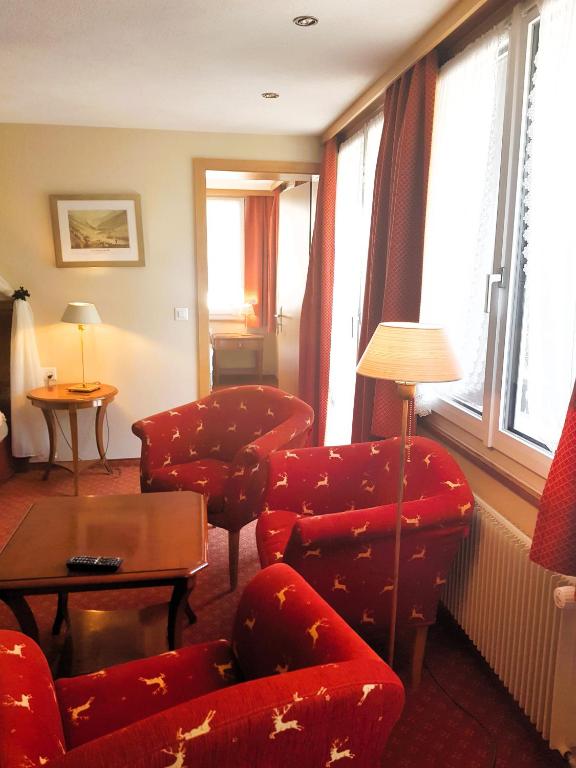 a living room with red chairs and a table and windows at Self-Service Guesthouse Berggeist in Saas-Fee
