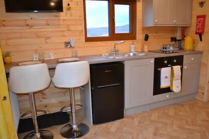 a kitchen with a sink and two bar stools at LetAway - The Hive Lodge at Ashes Farm in Settle