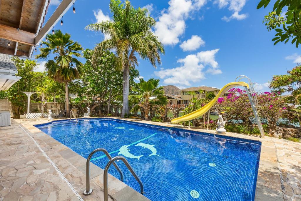 a swimming pool with a slide in a backyard with palm trees at Tranquil Marina Front Pool House Resort in Honolulu