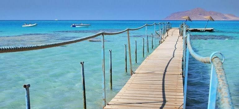 a wooden pier in the ocean with boats in the water at Red sea Hotel Marsa Alam in Marsa Alam City