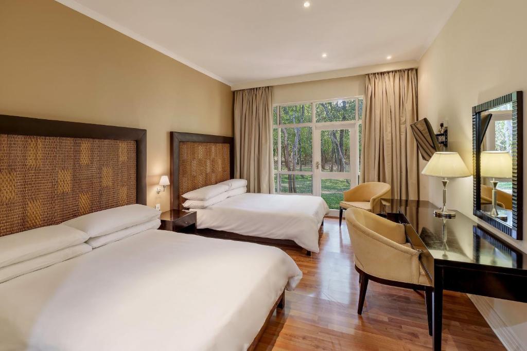 a hotel room with two beds and a desk and a television at Protea Hotel by Marriott Lusaka Safari Lodge in Chisamba