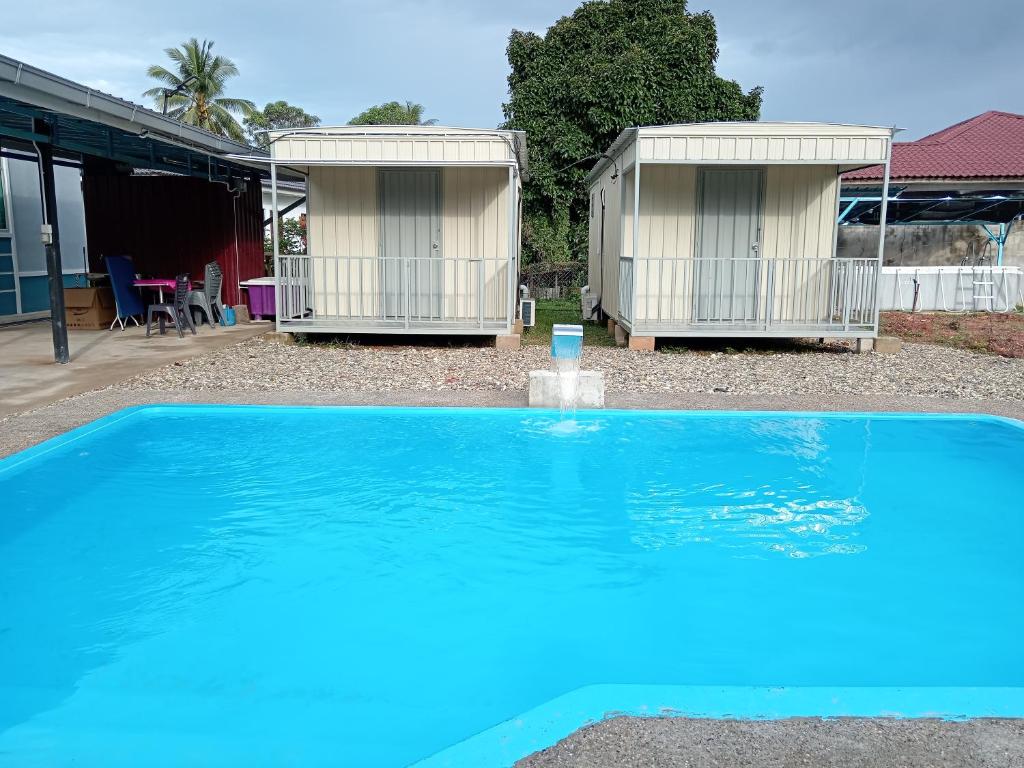 a blue swimming pool with two huts in the background at Homestay Pinang Tunggal Cabin in Sungai Petani