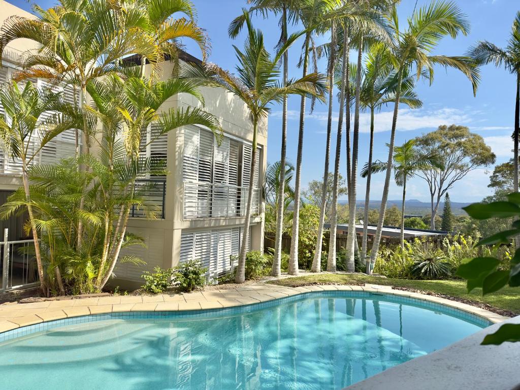 a swimming pool in front of a building with palm trees at Oasis Rooftop Spa Apartment in Noosa Heads
