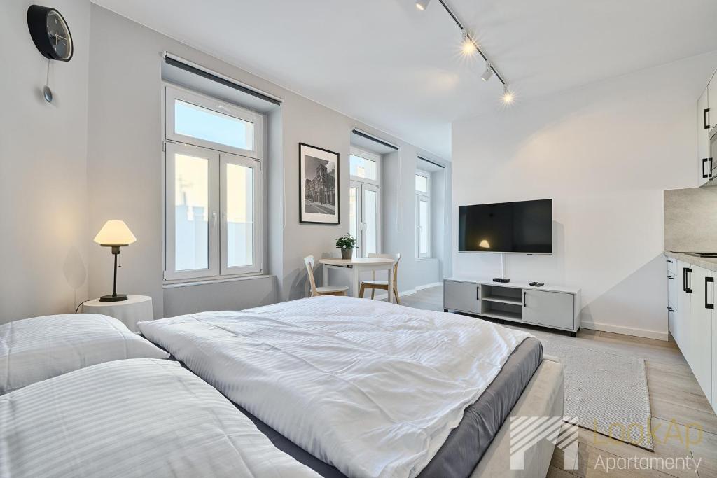 a white bedroom with a large bed and a tv at Polonia Residence III by LookAp Parking in Łódź