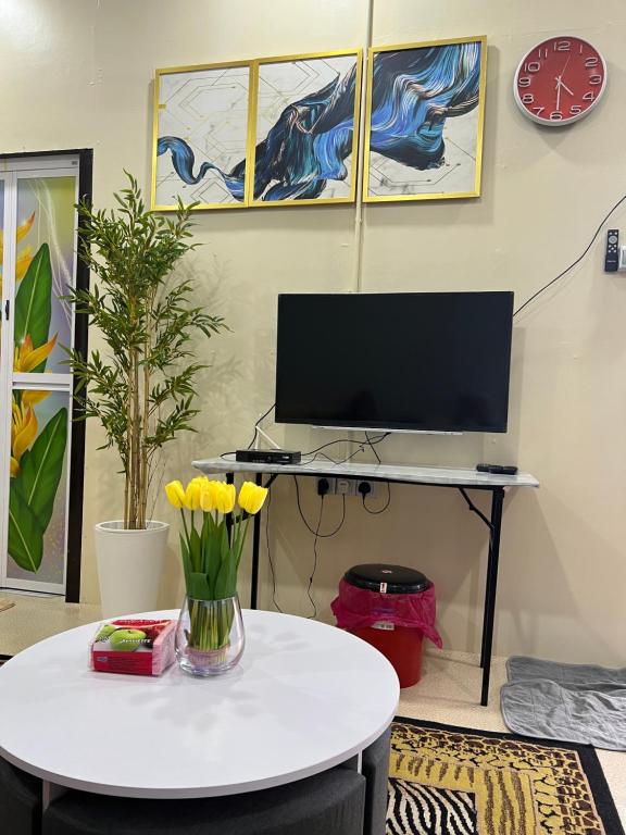 Cette chambre dispose d'une table avec une télévision et d'une table avec des fleurs. dans l'établissement Safiyya Homestay, à Kota Bharu