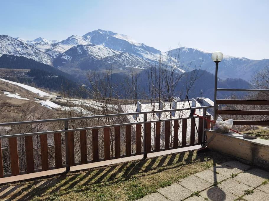 a wooden fence with snow covered mountains in the background at Il giardino sulle Piste in Prato Nevoso