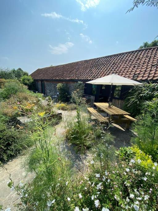 a picnic table with an umbrella in front of a house at Oyster Barn sleeps six, North Norfolk in Roughton