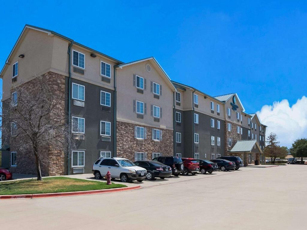 un gran edificio de apartamentos con coches aparcados en un aparcamiento en WoodSpring Suites Fort Worth Trophy Club, en Trophy Club