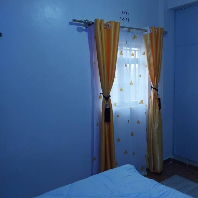 ein blaues Zimmer mit einem Bett und einem Fenster mit Vorhängen in der Unterkunft Aura's Airbnb in Busia