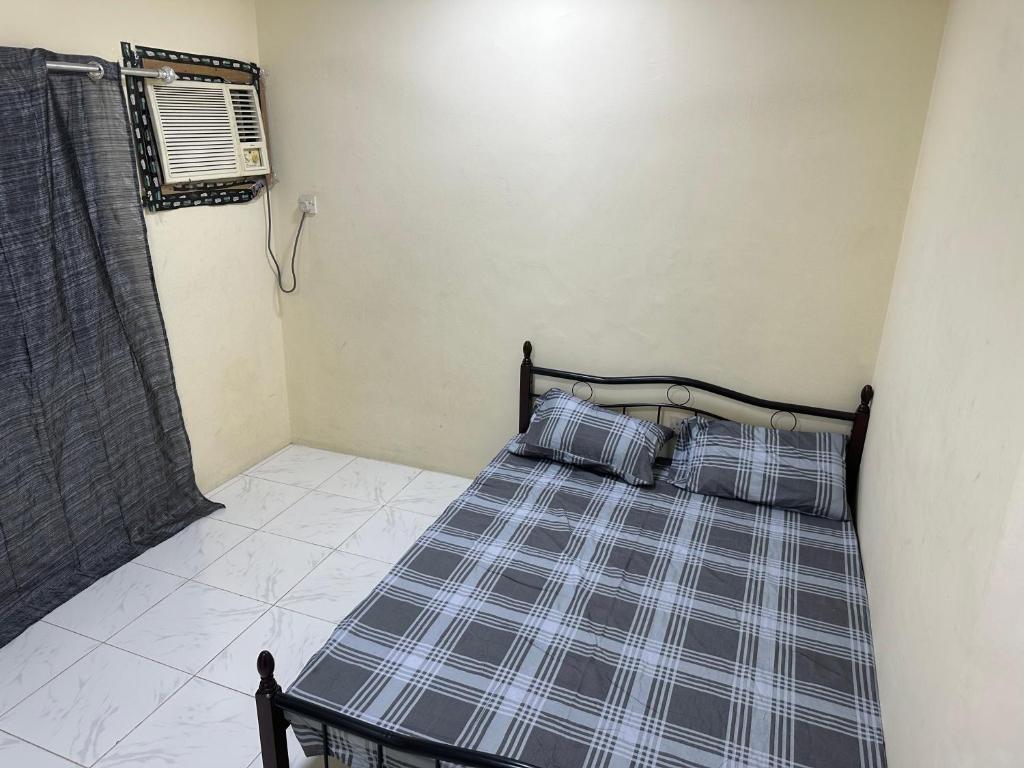 a small bedroom with a bed with plaid sheets at Room available in one bedroom appartment dating not allowd thare in Sharjah
