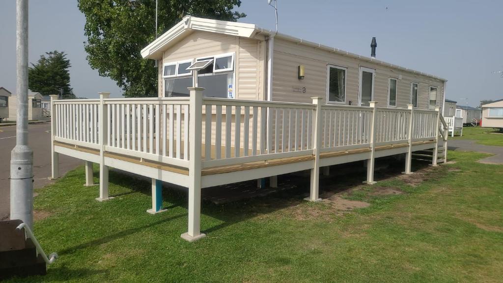a mobile home with a white railing and a porch at 8 Bed Sun Decked Caravan Unlimited High speed Wifi and fun at Seawick Holiday Park in Clacton-on-Sea