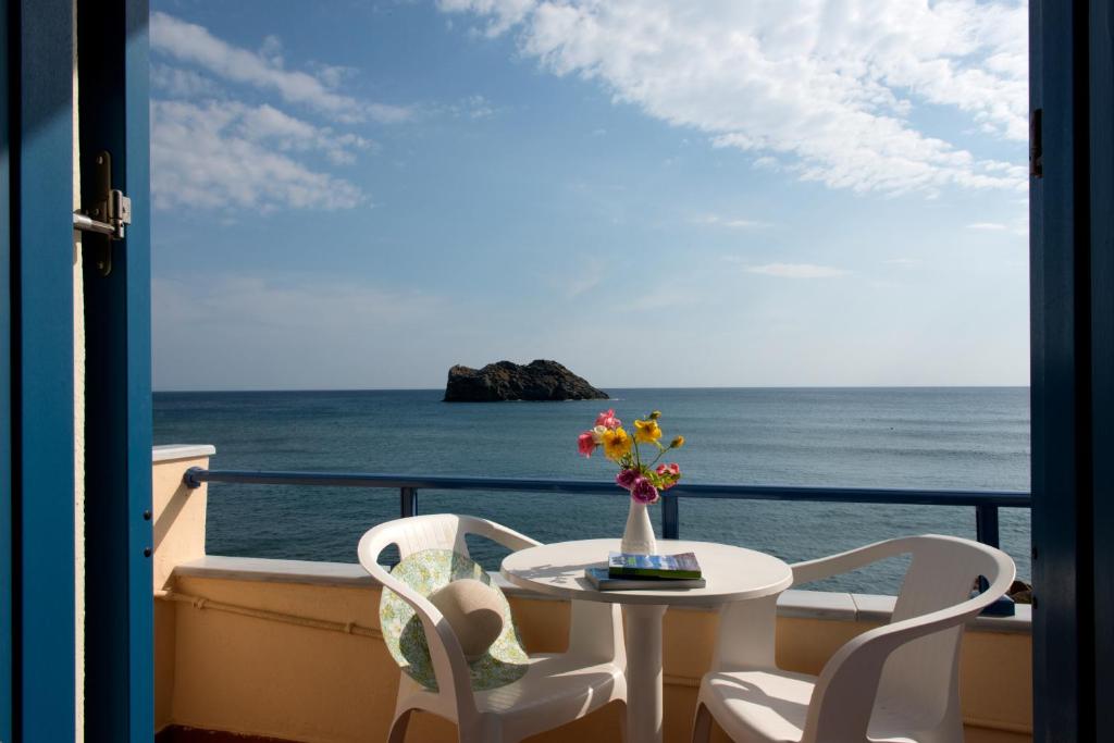 een tafel en stoelen op een balkon met uitzicht op de oceaan bij Hotel Kyma in Skala Eresou