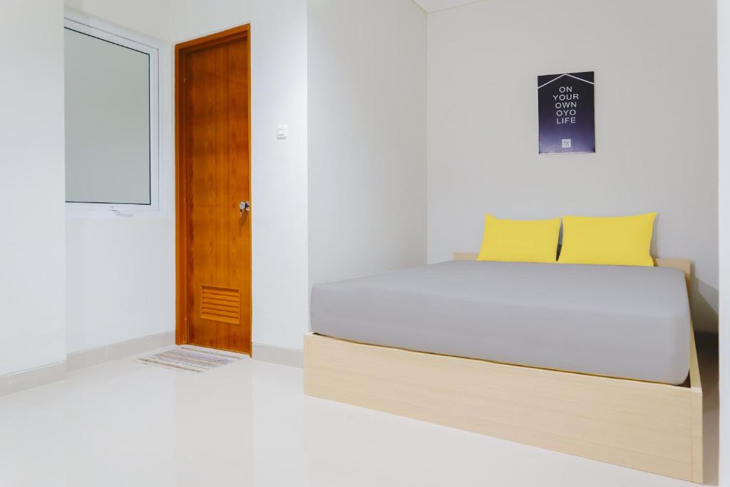 1 dormitorio con 1 cama con almohadas amarillas y puerta en OYO Life 1830 Mandala Residence, en Yakarta
