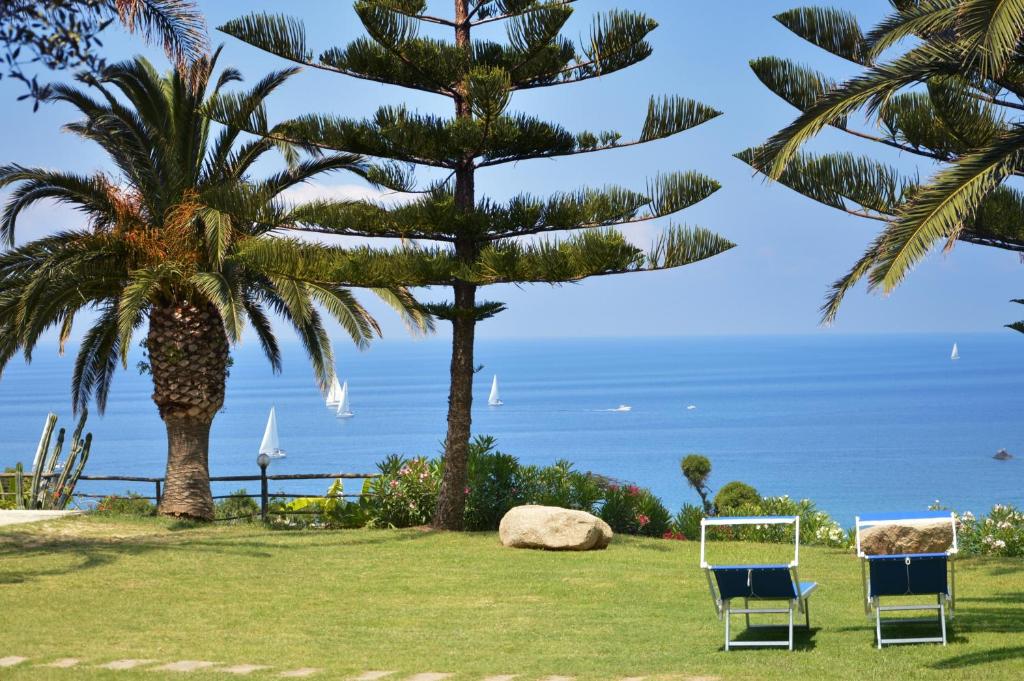 zwei Stühle auf einem Rasen mit einer Palme und dem Meer in der Unterkunft La Meridiana in Capo Vaticano