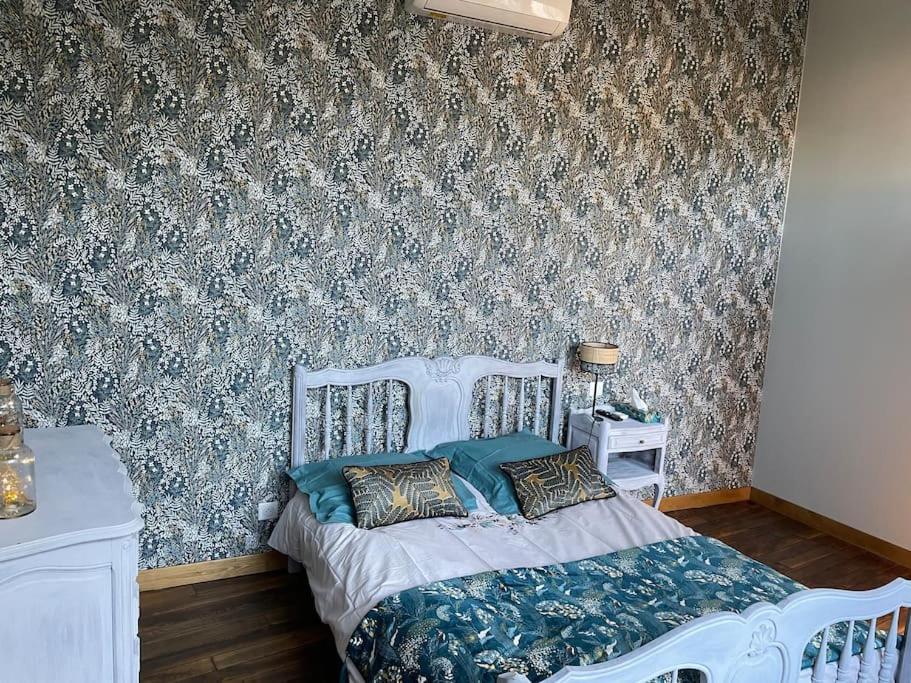 a bedroom with a white bed and a wall with wallpaper at Appartement de caractère in Mirecourt