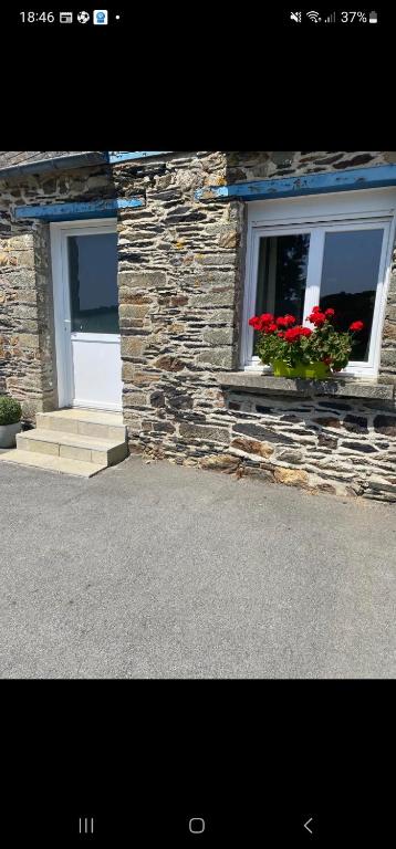 a stone building with two windows with red flowers at Studio du Quintinet in Le Quillio