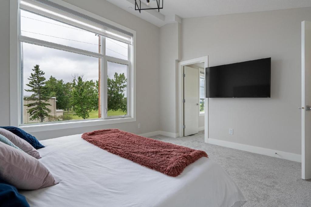 - une chambre blanche avec un grand lit et une télévision à écran plat dans l'établissement Modern Altadore Home 3 Br Fireplace Sleeps 8, à Calgary