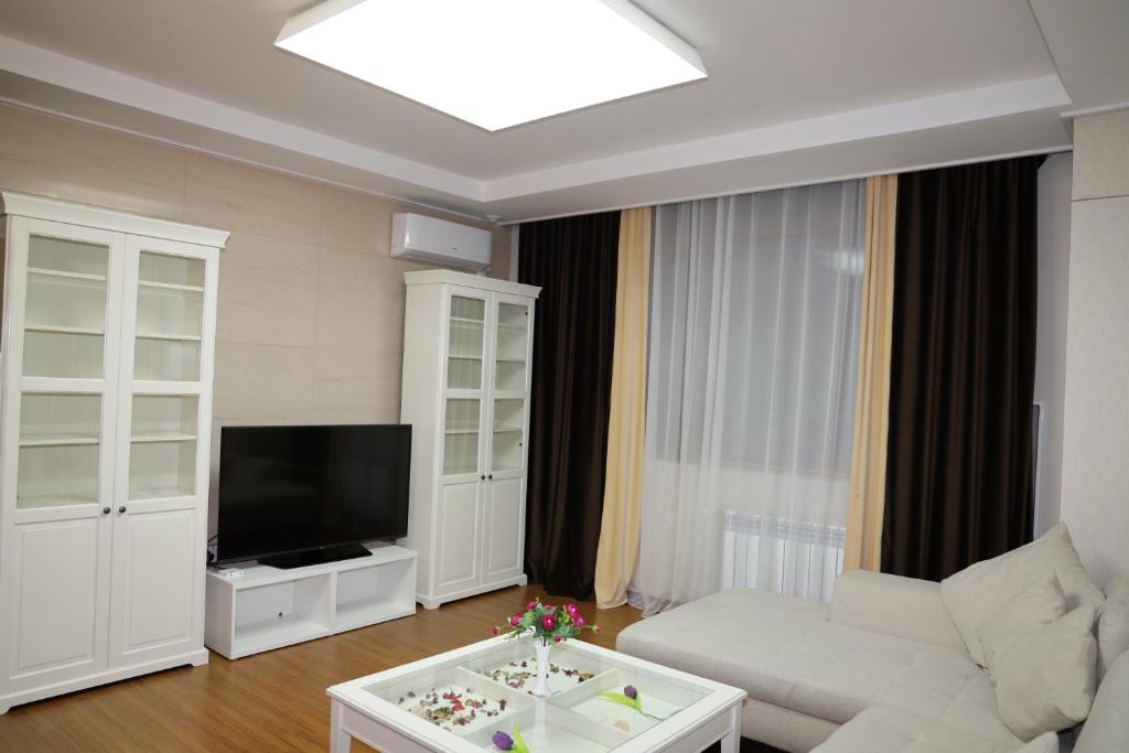 a living room with a white couch and a tv at Highvill Apartments in Astana