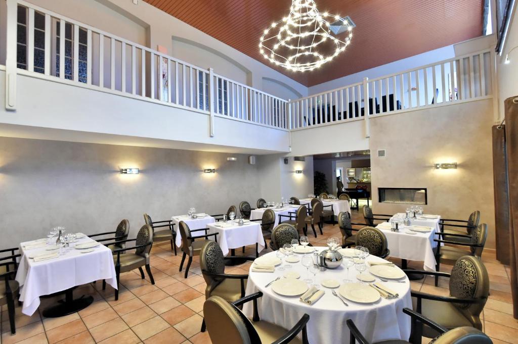 a restaurant with white tables and chairs and a chandelier at Le Domaine des Oliviers in Pierrelatte