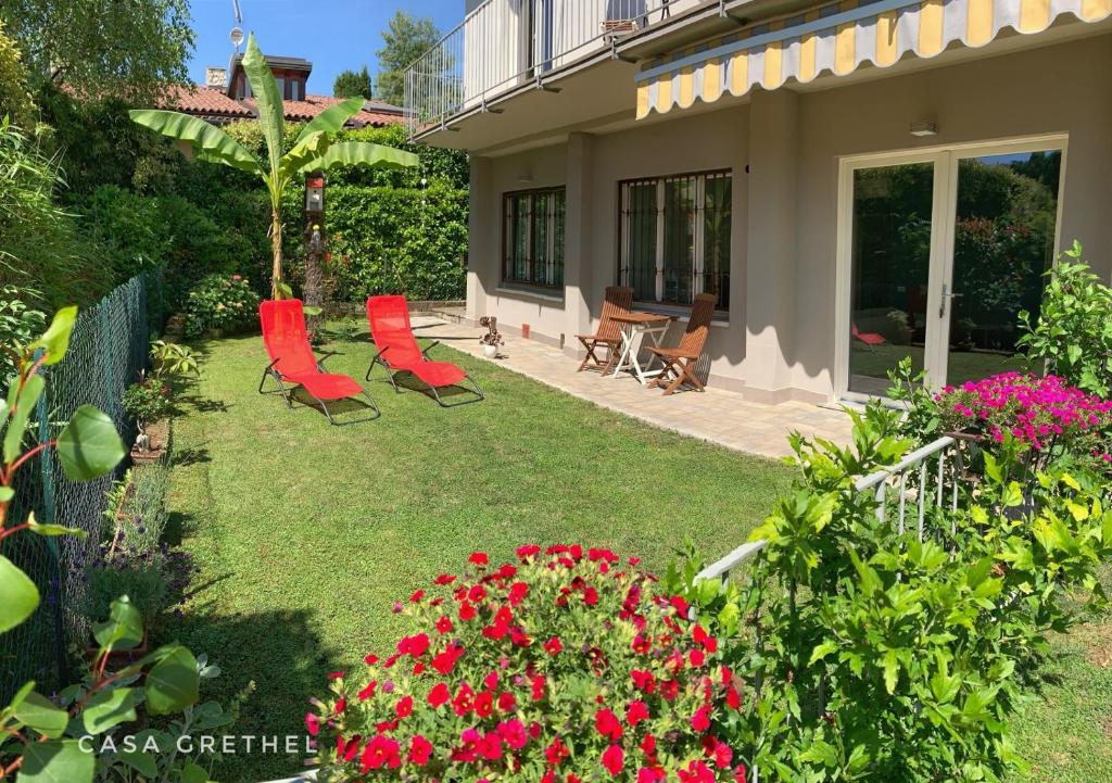 a garden with red chairs and flowers in a yard at Appartamento Grethel - Rebomaholidays in Gardone Riviera