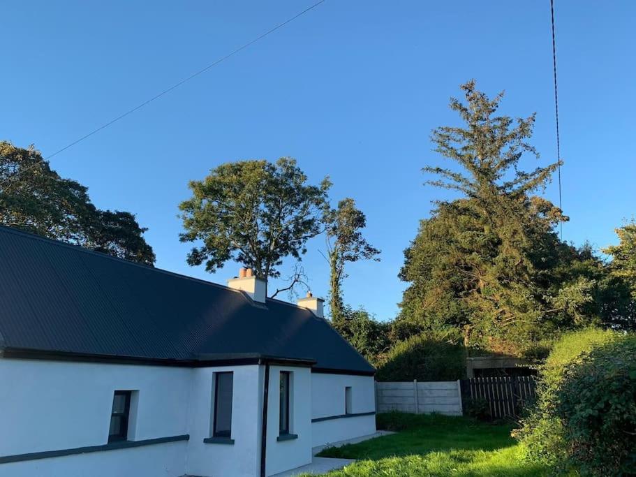 una casa bianca con tetto nero e alberi di Rose Cottage a Killarney