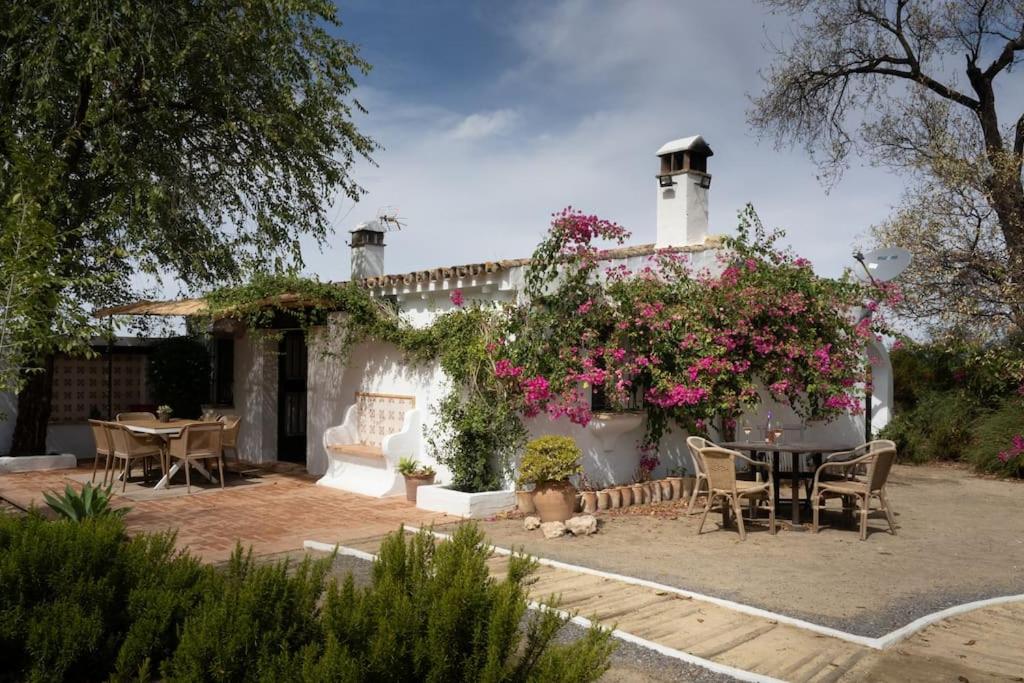 una casa con mesa, sillas y flores en Ranchito de Alhucemas,piscina privada y barbacoa, en Montellano