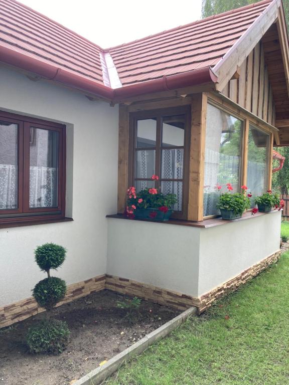 dom z dwoma oknami i kwiatami na nim w obiekcie Nyírfa-Lak Apartman w mieście Szilvásvárad