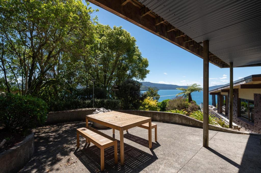 a wooden table and bench on a patio with a view of the water at Tironui Lake Tarawera in Lake Tarawera