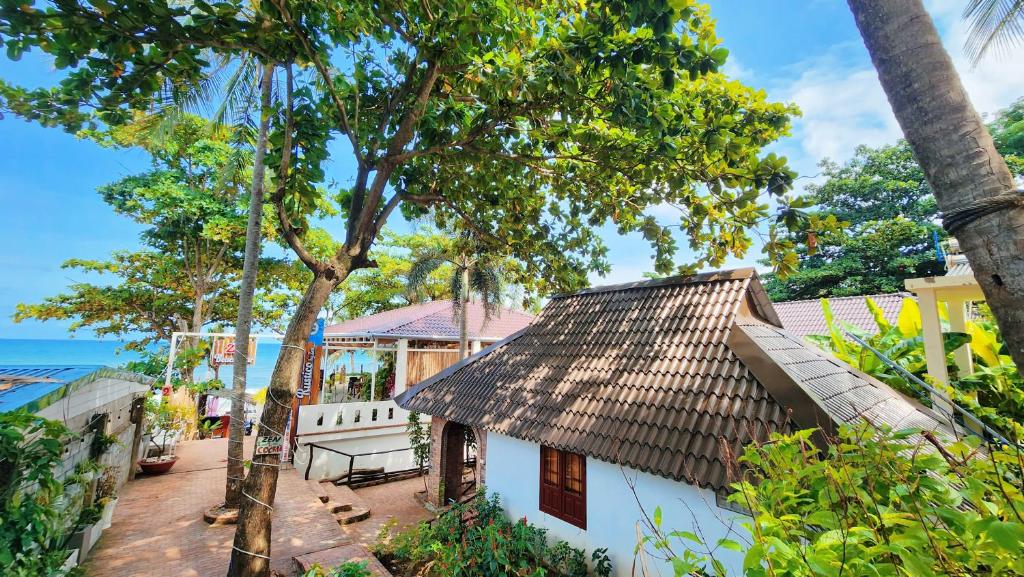 uma casa branca com telhado de palha e árvores em AND Resort em Duong Dong