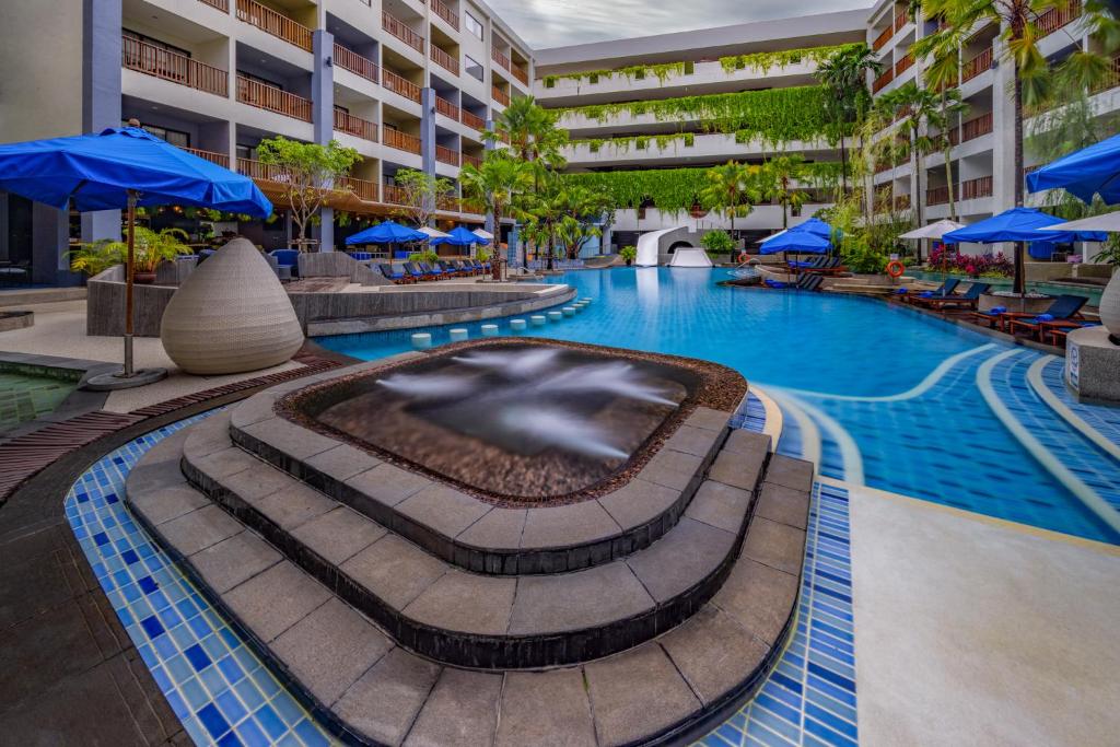 a swimming pool in a hotel with blue umbrellas at Deevana Plaza Phuket - SHA Extra Plus in Patong Beach