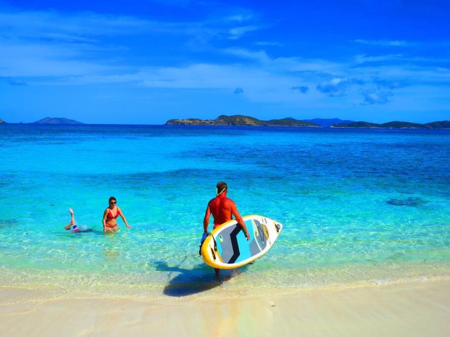 dos personas en el agua con una tabla de surf en una playa en Brand New Luxury Private Pool Villa Amber - 5 mins walk to #Sapphire Beach, en East End