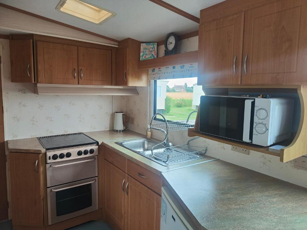 a kitchen with wooden cabinets and a microwave and a sink at The hobbits in Dymchurch