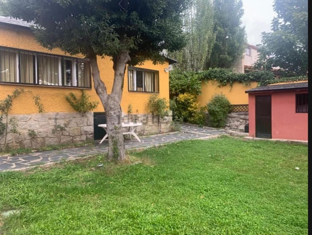 un giardino di fronte a una casa gialla con un albero di Casita roja a Cercedilla