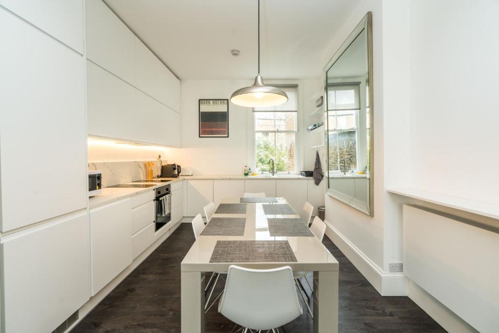 uma cozinha com uma mesa longa e armários brancos em Stylish 2 bedroom at Hammersmith em Londres