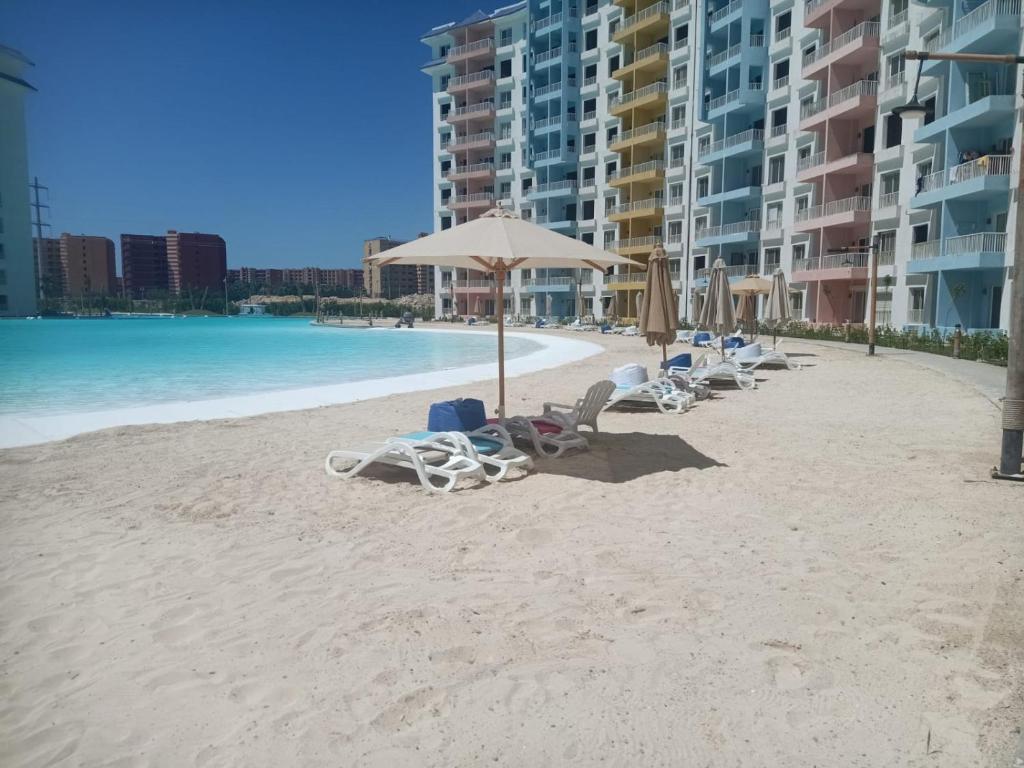 a beach with chairs and umbrellas and the ocean at Two Bedrooms for Families only Chalet Sia Lagoon Golf Porto Marina للعائلات فقط شاليه غرفتين كريستال لاجون جولف بورتو مارينا in El Alamein
