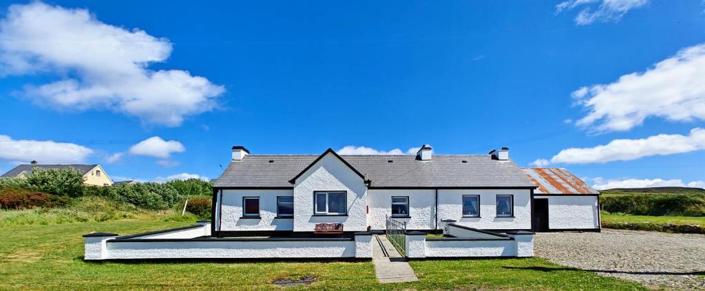 a white house on a field with a blue sky at Teach Róisin-Traditional Irish holiday cottage in Malin Head. in Malin