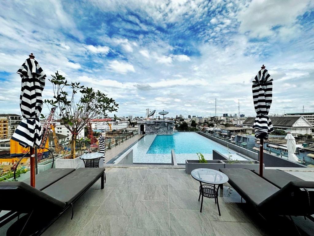 Rooftop pool seating with loungers, striped umbrellas and a Bangkok skyline view.