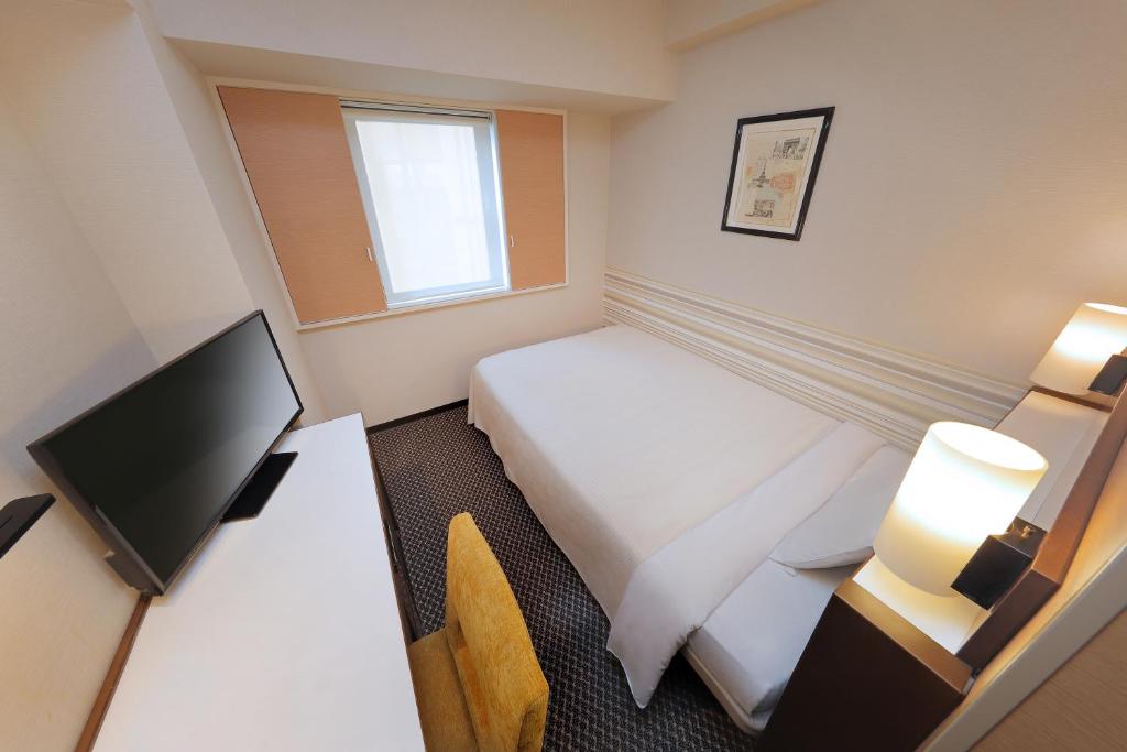 a hotel room with a bed and a desk with a television at Keio Presso Inn Shinjuku in Tokyo
