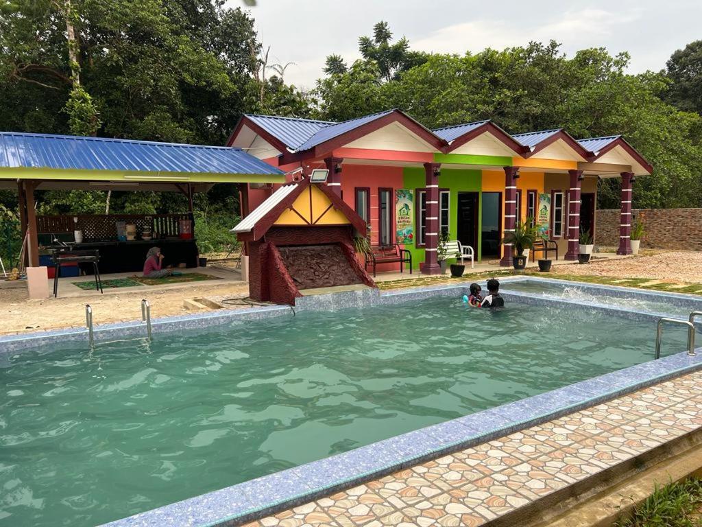 two people swimming in a pool in front of a house at D'DUSUN RAUDHAH HOMESTAY in Baling