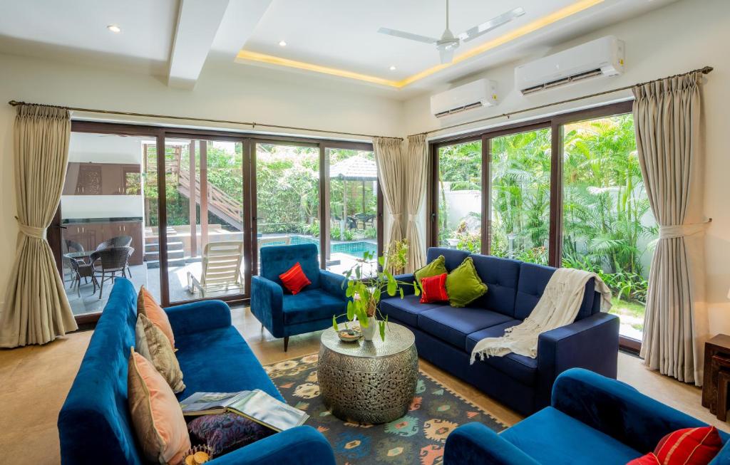 a living room with blue furniture and large windows at Elivaas Indah Luxe 4BHK Villa with Pvt Pool, Moira in Old Goa