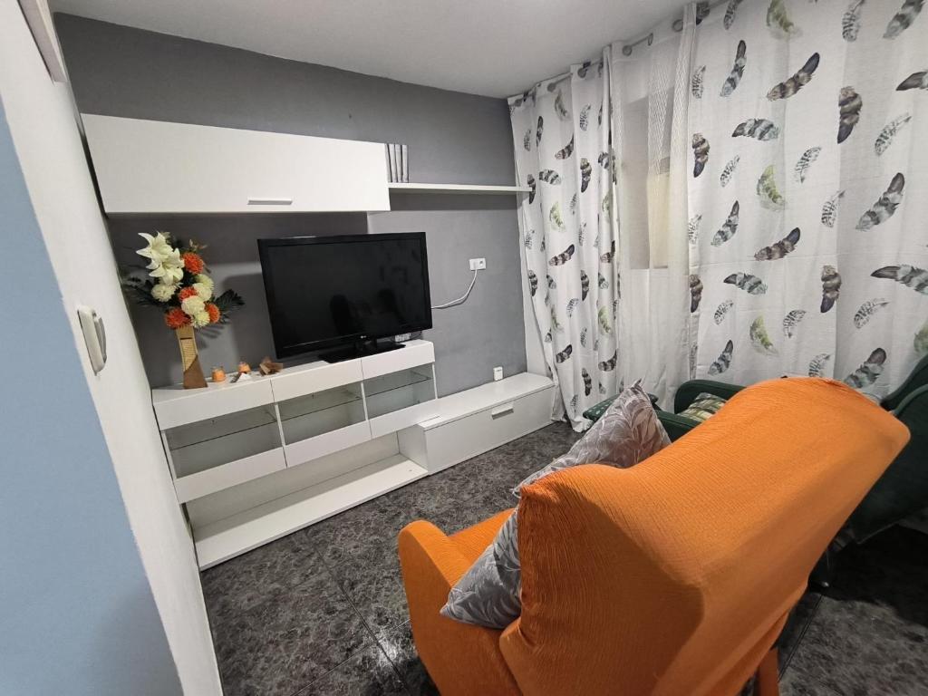 sala de estar con silla naranja y TV en La casa del Viajero, en Puertollano