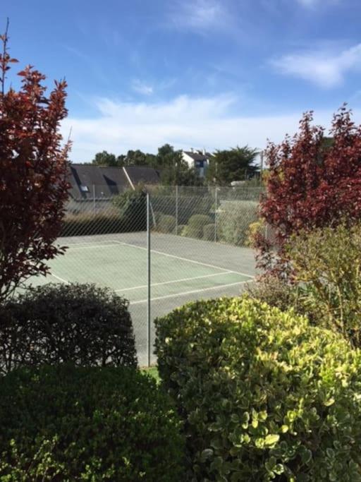 a tennis court with a net and some bushes at Plage de rêve et tennis devant la maison in Pornichet