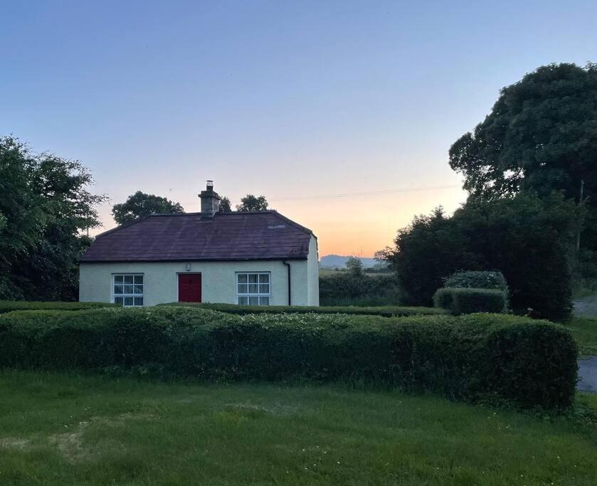 een wit huis met een rode deur in een veld bij The Gate-Lodge at Levally House in Monea