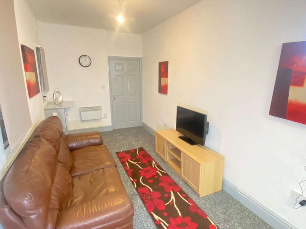 a living room with a brown leather couch and a television at SEV Apartments Wakefield in Hemsworth