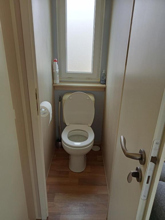 a small bathroom with a toilet with a window at Stacaravan met eigen terras en tuin 6personen in Bredene